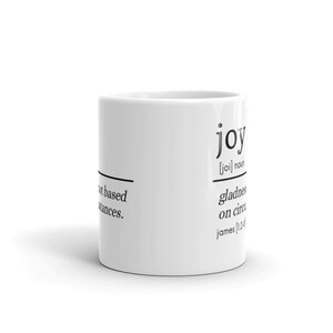 May include: White ceramic mug with a black and white definition of the word "joy" printed on the side. The definition reads: "[joi] noun gladness not based on circumstances. james 1:2-4"