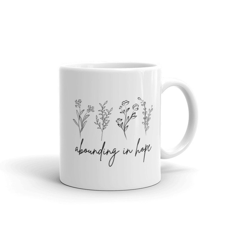 May include: White ceramic mug with a black line drawing of five flowers and the text "abounding in hope".