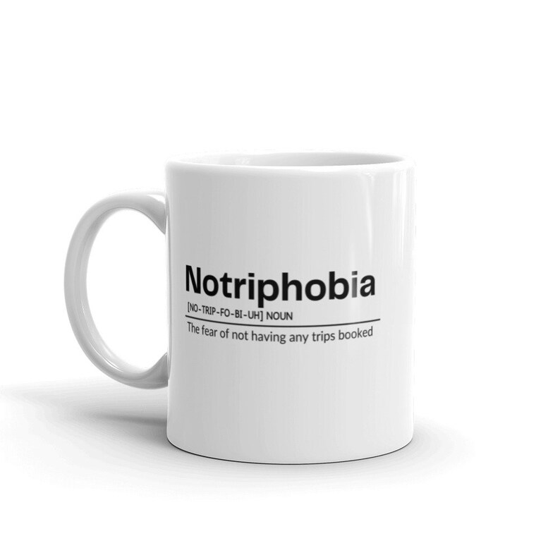 May include: White ceramic coffee mug with black text that reads "Notriphobia [NO-TRIP-FO-BI-UH] NOUN The fear of not having any trips booked"
