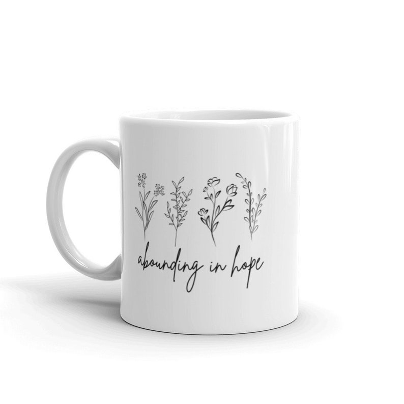 May include: White ceramic mug with a black line drawing of five flowers and the text "abounding in hope".