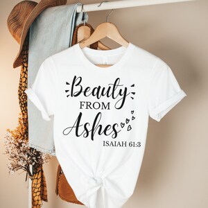 May include: White t-shirt with the text "Beauty from Ashes" and the Bible verse "Isaiah 61:3" printed in black.