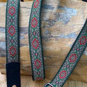 Peut inclure: Une sangle de guitare noire avec un motif vert, rouge et or. La sangle a une extrémité en cuir noir avec une boucle en métal.