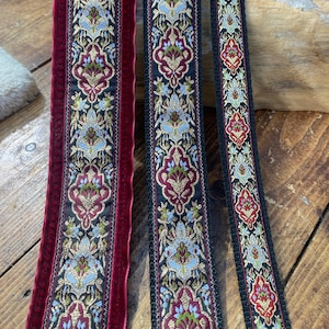 May include: Close-up of three decorative ribbons with ornate floral patterns. The ribbons feature a color palette of burgundy, black, gold, and light blue. One ribbon has a velvet texture. The word "VEGAN" is displayed in a white box.