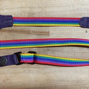 May include: A rainbow striped camera strap with purple leather ends and metal clasps.