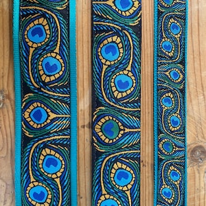 May include: Three strips of fabric with a peacock feather pattern. The fabric is black with blue, green, and gold accents. The fabric is trimmed with a turquoise blue border.