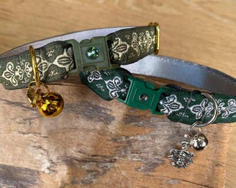 Pode incluir: Dois colares de gato com padrão verde e prateado com pingentes de sino. Os colares têm fivelas ajustáveis e são decorados com um design de flor de lis.