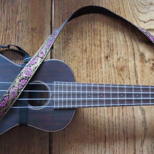 May include: A brown ukulele with a floral patterned strap. The ukulele has a black strap attached to the body and a white string.
