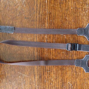 May include: Two brown leather camera straps with adjustable buckles. One strap has a metal button and the other has a metal ring.