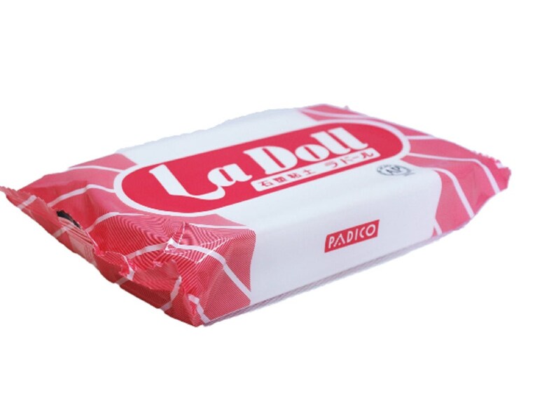 Op de afbeelding: Een roze en witte verpakking La Doll polymer clay, een merk van modelleerklei. De verpakking heeft de tekst "La Doll" in rode letters en de tekst "PADICO" in zwarte letters.