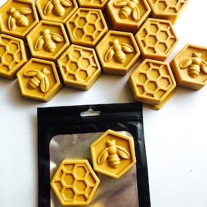 May include: A collection of hexagonal honey-coloured soaps with a bee design. The soaps are arranged in a honeycomb pattern. Some soaps are in a black and silver bag.