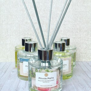 May include: A set of six clear glass bottles with silver lids and reed diffusers. The bottles are filled with a clear liquid and have labels that say "Minnie Melts Wild Rhubarb & Mint Reed Diffuser" and "www.minniemelts.co.uk".