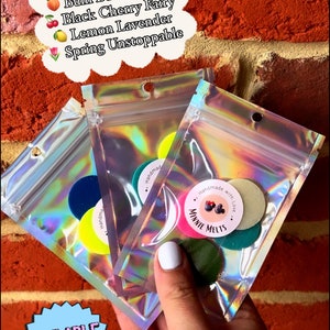 May include: Four packs of scented wax melts in clear plastic bags. The wax melts are in various colours, including green, pink, and yellow. The bags are labelled with the text "Handmade with Love" and "Minnie Melts".