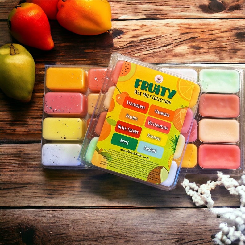 Może przedstawiać: Przezroczysty plastikowy pojemnik wypełniony kolorowymi woskowymi kostkami. Pojemnik ma etykietę z napisem "Fruity Wax Melt Collection" z listą zapach&oacute;w owocowych: truskawka, brzoskwinia, czarna wiśnia, jabłko, mandarynka, arbuz, ananas, kokos.