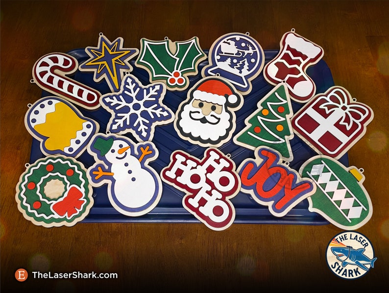 May include: A collection of 15 wooden Christmas ornaments with various designs, including a candy cane, a star, holly, a snowflake, Santa Claus, a Christmas tree, a gift box, a bell, a snowman, a wreath, the words "Ho Ho Ho", the word "Joy", and a green ornament with a diamond pattern.