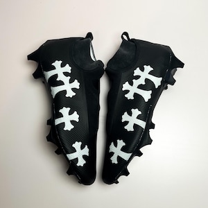 May include: A pair of black soccer cleats with white cross designs. The cleats have a sock-like fit and a textured upper.