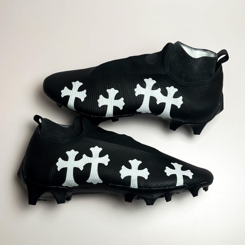 May include: A pair of black soccer cleats with white cross designs. The cleats have a sock-like design and are made of a synthetic material.