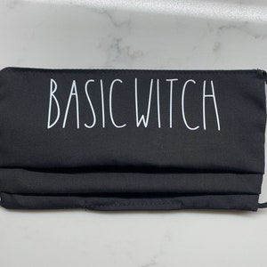May include: Black face mask with white text that reads "BASIC WITCH".