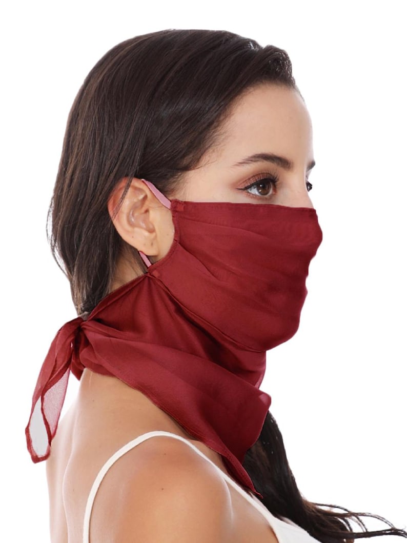 May include: A deep red, semi-sheer fabric face covering designed with a triangular scarf-like shape that extends down the neck. The mask features thin, light-coloured elastic ear loops to secure the lightweight material over the nose and mouth.