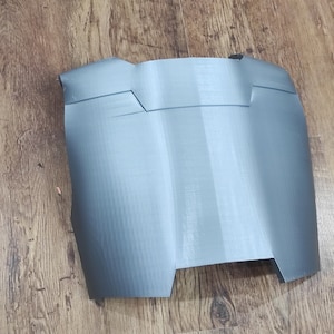 May include: A gray plastic 3D printed piece with a curved shape and a textured surface. The piece has two raised lines on the top and a small indentation in the center.