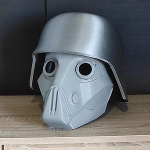 May include: A gray 3D printed helmet with a visor and a face mask. The helmet has a rounded top and a flat brim.