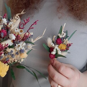 May include: Two bouquets of dried flowers, one large and one small. The larger bouquet features yellow, red, and white flowers, while the smaller bouquet features yellow, red, and white flowers with a hint of lavender.