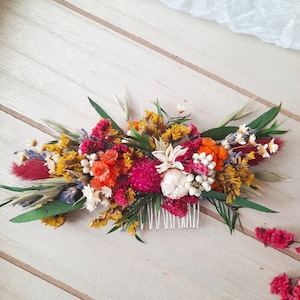 May include: A floral hair comb with dried flowers in shades of pink, orange, yellow, and white. The comb is made of metal and has a delicate design.
