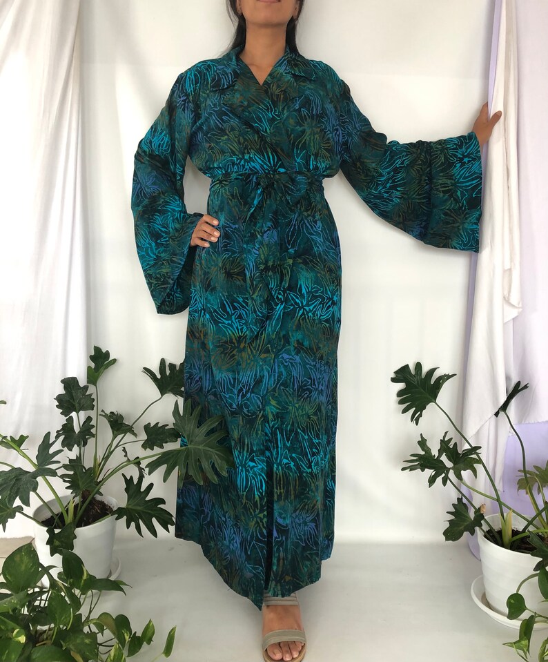May include: A long, teal blue robe with a floral print and a tie belt. The robe has long sleeves with wide cuffs.