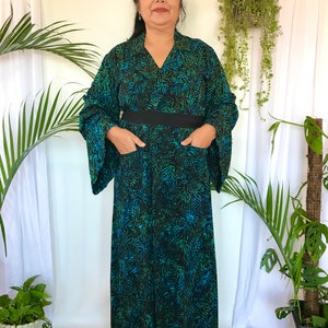 May include: A long, black and green patterned dress with a black belt and pockets. The dress has a V-neck and long sleeves.
