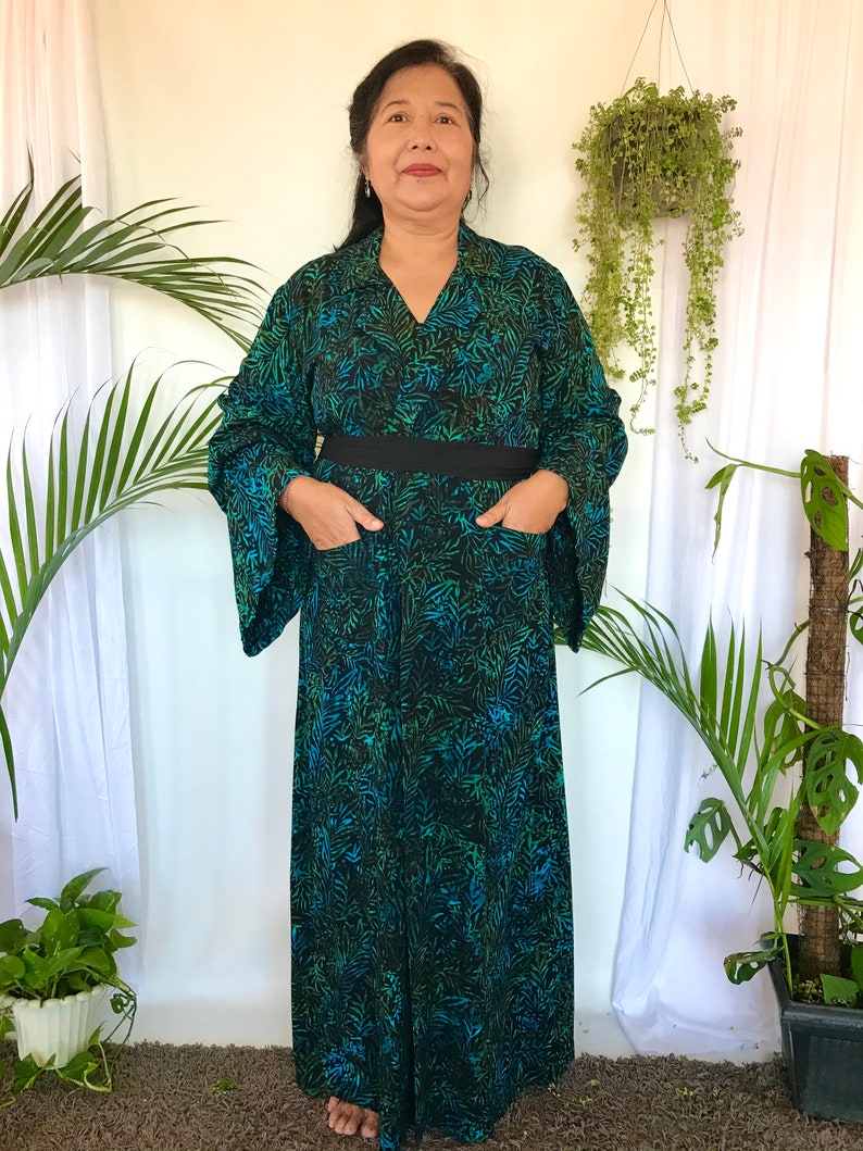May include: A long, black and green patterned dress with a black belt and pockets. The dress has a V-neck and long sleeves.
