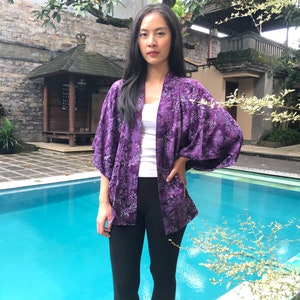 May include: A woman wearing a purple floral kimono with a white top and black leggings. She is standing by a swimming pool.