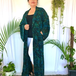 May include: A long, black and green patterned robe with a collar and long sleeves. The robe is open in the front and the person wearing it is standing on a brown carpet.
