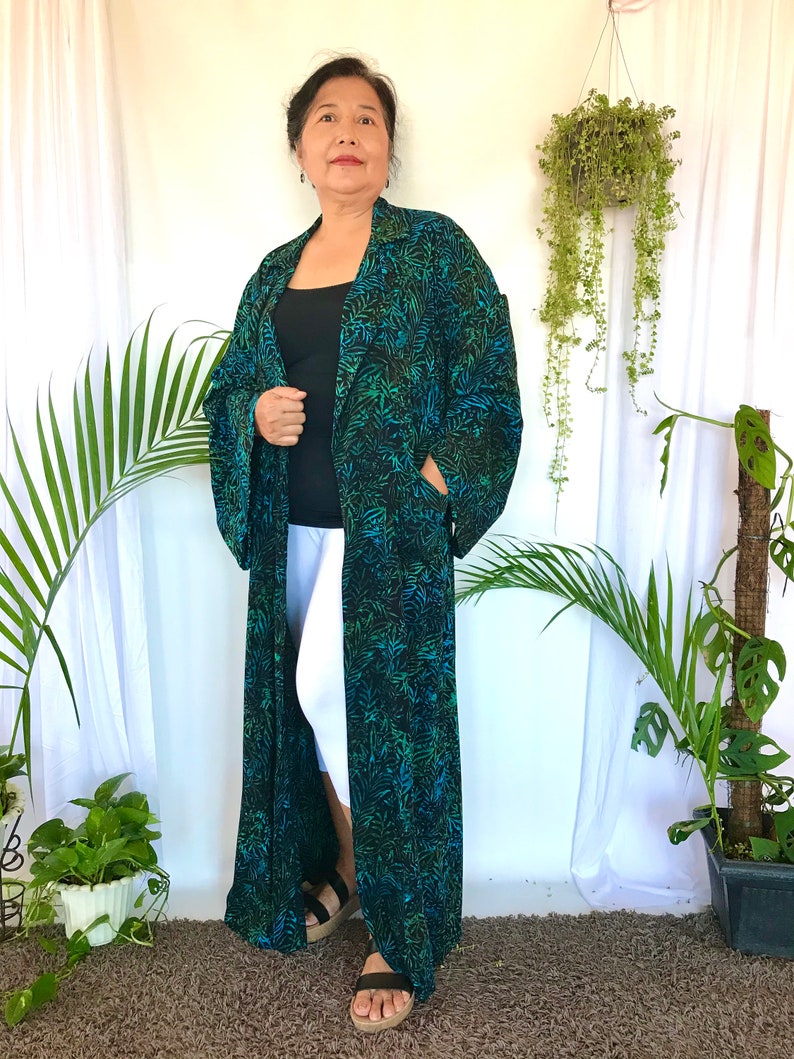 May include: A long, black and green patterned robe with a collar and long sleeves. The robe is open in the front and the person wearing it is standing on a brown carpet.