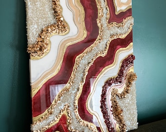 May include: Abstract art painting with red, white, and gold colors. The painting features a swirling, agate-like design with gold glitter and white crystals.