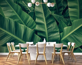 May include: A dining room with a white table and eight wooden chairs. The wall is covered with a tropical wallpaper featuring large green banana leaves.