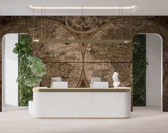 Puede incluir: Un mostrador de recepción blanco con un borde dorado se encuentra frente a una pared con un papel tapiz de mapa del mundo vintage. El mapa está en tonos marrones y beige y tiene un diseño de rompecabezas. Se pueden ver plantas verdes a ambos lados del mostrador.