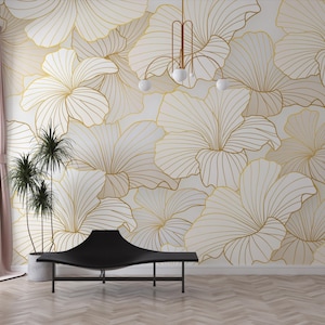 May include: A white wall with a gold floral pattern wallpaper. The wallpaper features a repeating pattern of large, stylized flowers with thin, gold lines. A black, modern bench sits in front of the wall.