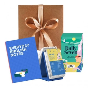 以下が含まれることがあります： 金色のリボンで結ばれた茶色の箱、"EVERYDAY ENGLISH NOTES"のテキストが入った青いノート、卓上カレンダー、"Daily Seven"のテキストが入った緑色の箱が特徴のギフトセット。英語学習用です。