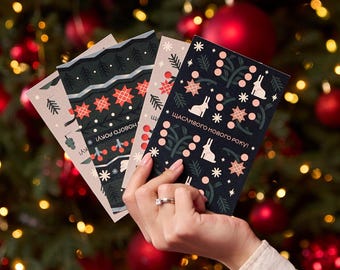 Könnte beinhalten: Eine Hand hält vier Weihnachtskarten mit festlichen Mustern. Die Karten zeigen Designs mit Sternen, Hasen und Schneeflocken in Rot, Weiß und Schwarz. Der Text "Frohes neues Jahr" ist auf einer Karte zu sehen.
