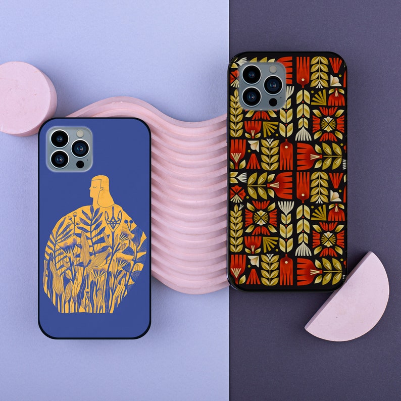 May include: Two phone cases with different designs. The first case is blue with a white outline of a person standing in a field of flowers. The second case is black with a geometric pattern of red, yellow, and green flowers.
