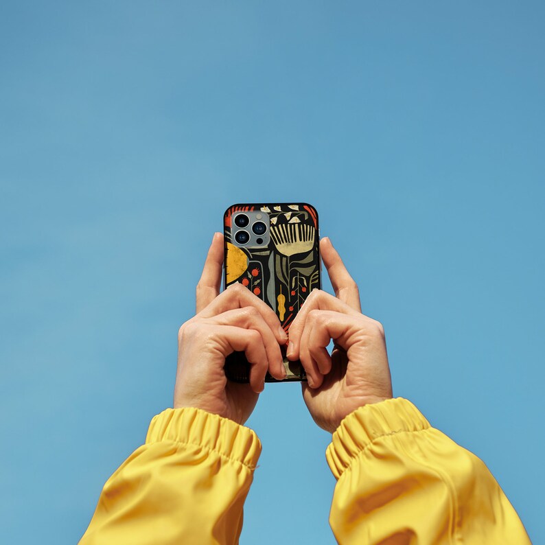 May include: A person is holding a black iPhone with a colorful floral pattern case. The phone is being held up to the sky, which is a bright blue.