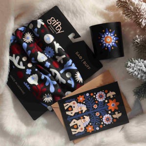 May include: A black headband with a floral pattern in red, white, and blue, a black mug with a star design, and a greeting card with a horse and floral design. The items are on a white, fluffy surface.