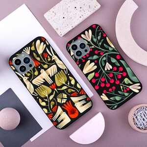 May include: Two black phone cases with a floral design. One case has a white and yellow floral design with red accents. The other case has a green and white floral design with red accents.