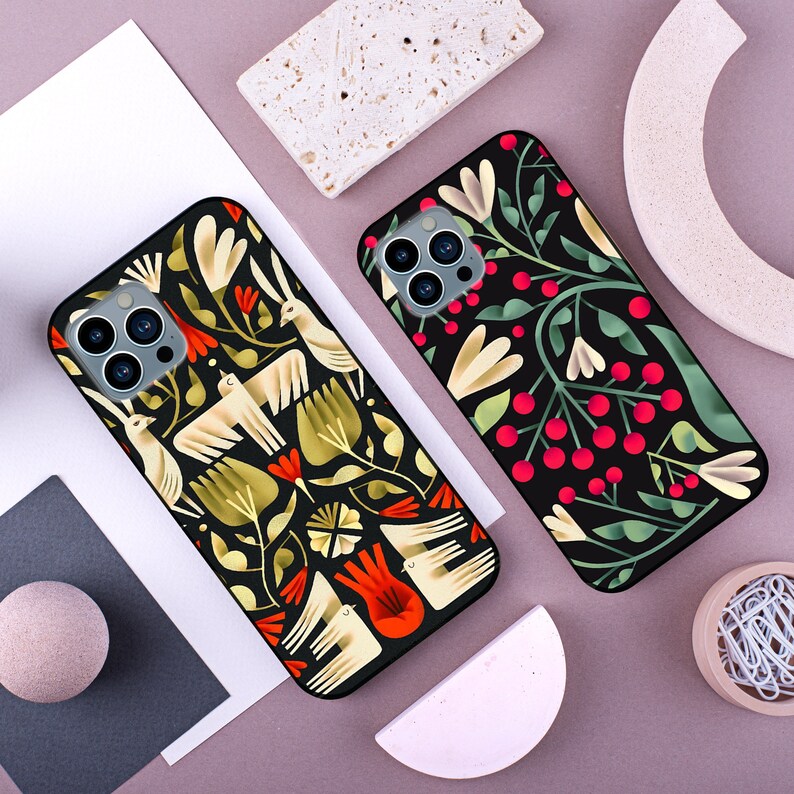 May include: Two black phone cases with a floral design. One case has a white and yellow floral design with red accents. The other case has a green and white floral design with red accents.