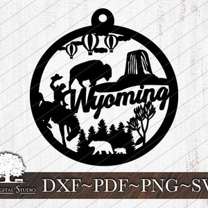 May include: Black and white silhouette of a Wyoming ornament with a cowboy riding a horse, a buffalo, a mountain, hot air balloons, and the word "Wyoming".