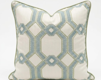 May include: A square throw pillow featuring an off-white base fabric with a repeating geometric pattern embroidered in light blue and sage green thread. The design consists of interconnected octagons and diamonds, finished with sage green piping.