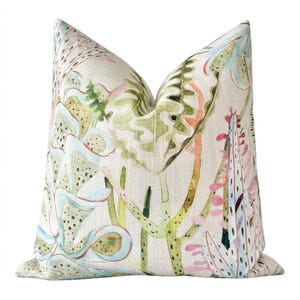 May include: A square throw pillow featuring a light beige linen-textured fabric printed with a botanical pattern of stylized succulents and cacti in shades of sage green, soft pink, pale blue, and dark olive green with fine dotted details.