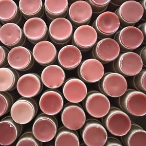 May include: A close-up view of a large group of lip balm tubes. The tubes are made of cardboard and have a pink lip balm inside. The lip balms are arranged in a circular pattern.