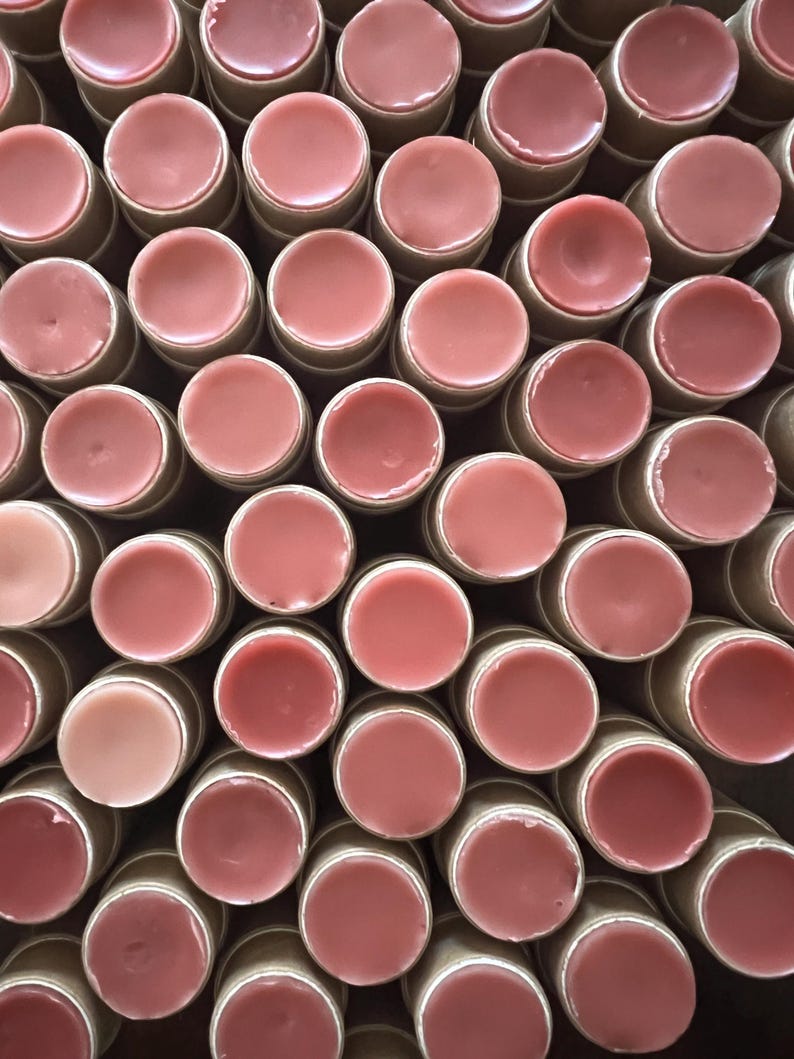 May include: A close-up view of a large group of lip balm tubes. The tubes are made of cardboard and have a pink lip balm inside. The lip balms are arranged in a circular pattern.