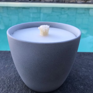 May include: A gray ceramic candle holder with a white candle and a white wick. The candle holder is sitting on a black surface.