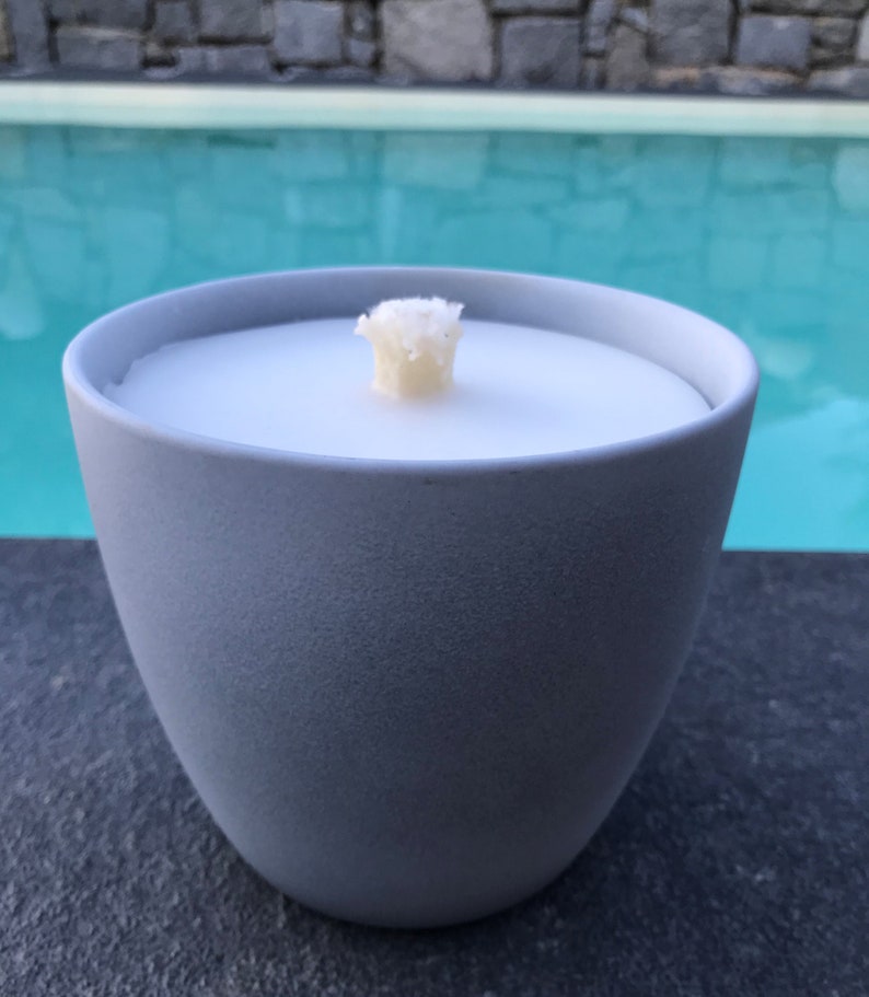 May include: A gray ceramic candle holder with a white candle and a white wick. The candle holder is sitting on a black surface.